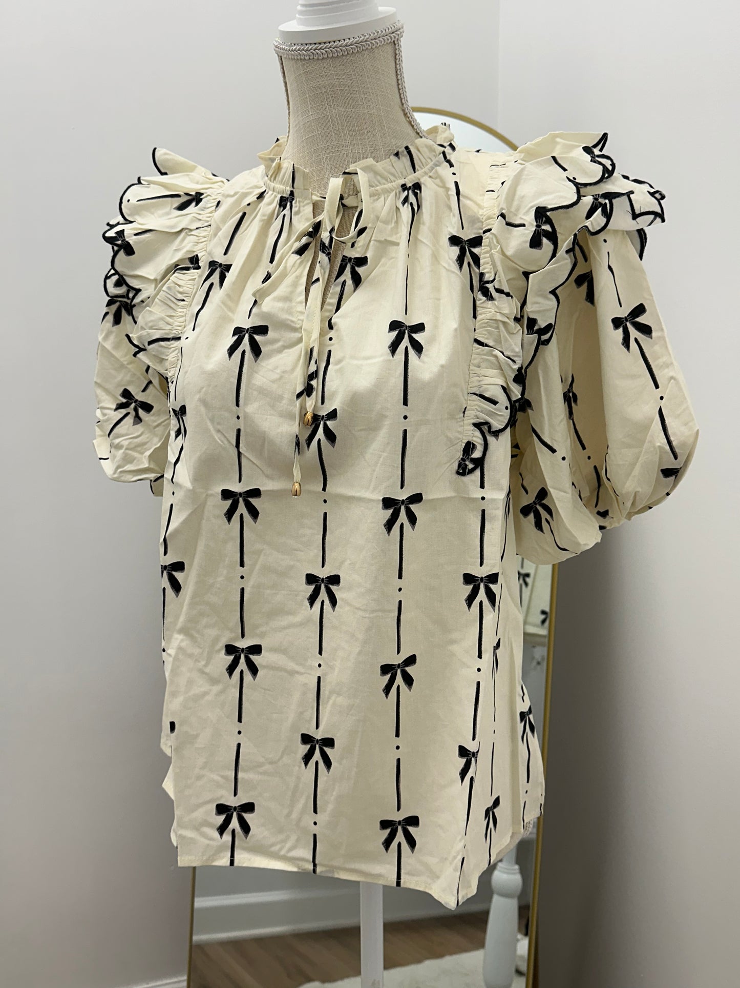 Bow print short puff sleeve v-neck top featuring tiered scallop delay at shoulders. Self-tie detail at ruffled neckline. Unlined. Woven. Non-sheer. Lightweight.